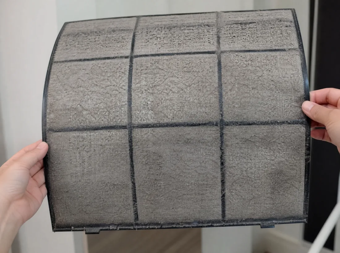 Hands holding an AC filter coated in a thick layer of gray dust, before cleaning
