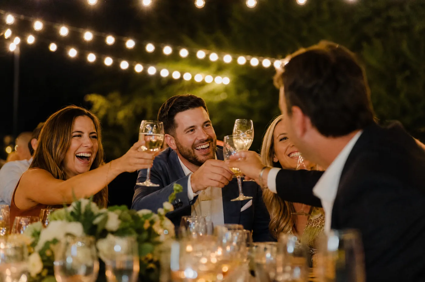 Guests laughing and raising glasses at a warmly lit evening event