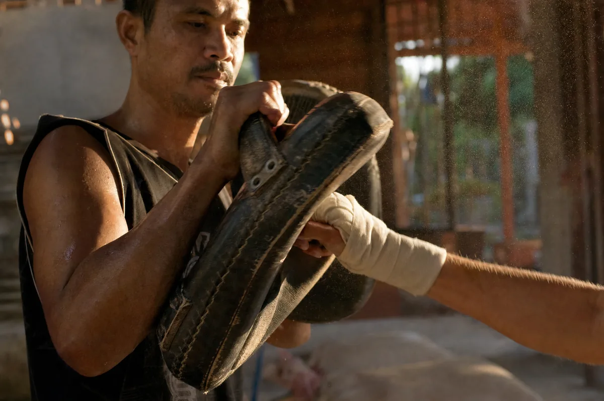 A trainer holding Thai kick pads as a wrapped fist presses in