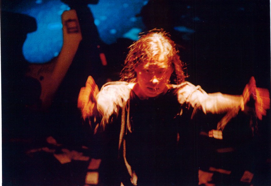 Narumol Kop Thammapruksa in performance, arms lifted against a cool projected background.