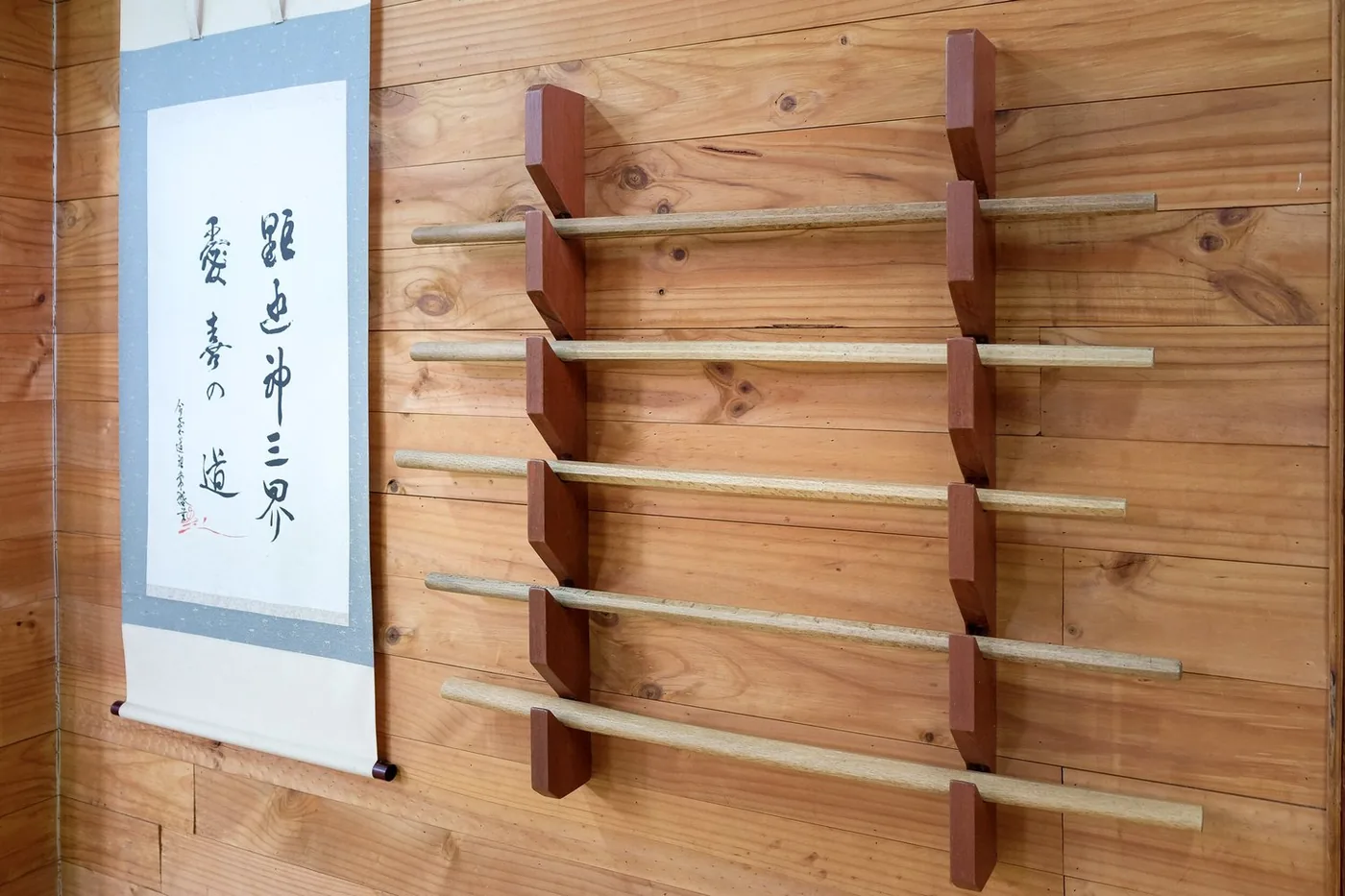 Wooden practice weapons on a rack beside a calligraphy scroll on the dojo wall